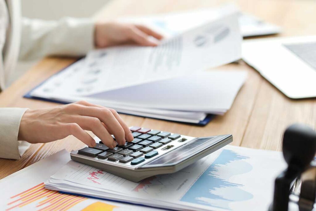 A business owner at a desk organizing receipts and entering expenses into a laptop with paperwork spread out.