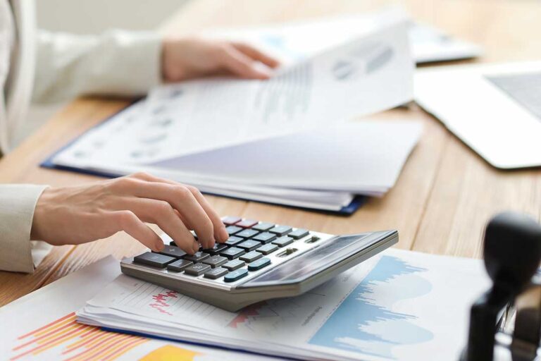A business owner at a desk organizing receipts and entering expenses into a laptop with paperwork spread out.