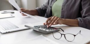 A person with a laptop and notebook reviewing receipts and financial notes at a kitchen table.