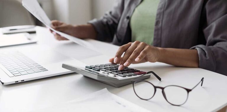 A person with a laptop and notebook reviewing receipts and financial notes at a kitchen table.
